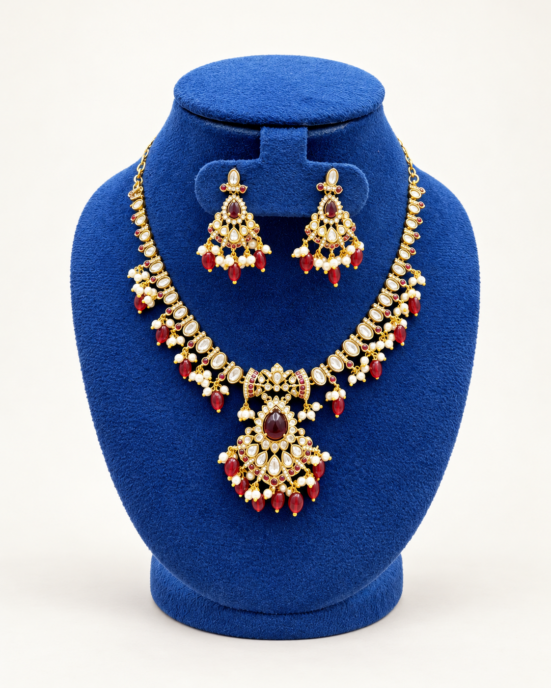 Kaveri kundan style beaded necklace set with earrings in maroon on a blue velvet display stand